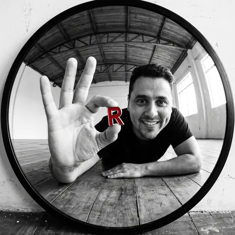 André segurando um R vermelho, refletido num espelho redondo